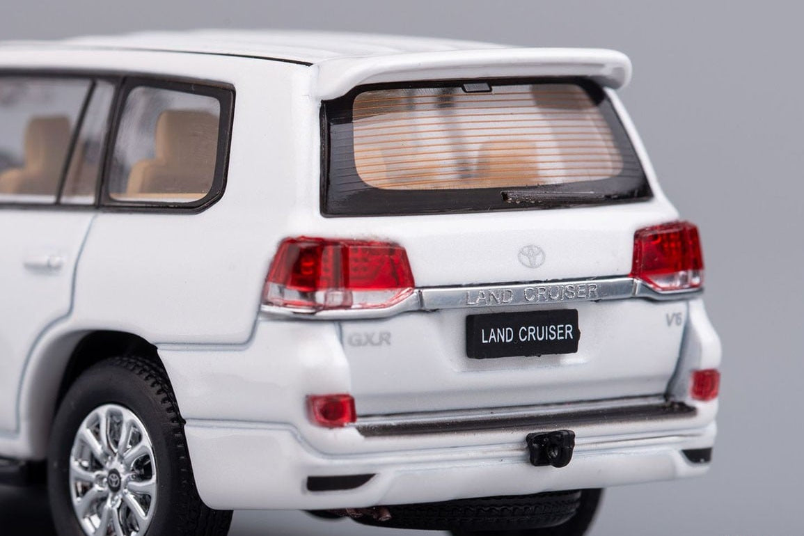 Close-up rear view of a white die-cast model car, specifically a Toyota Land Cruiser, on a neutral gray background.